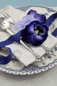 蓝色图案复古盘子古董银器和三色堇花放在蓝色桌布上图片