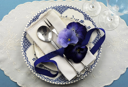 蓝色图案复古盘子古董银器和三色堇花放在蓝色桌布上图片