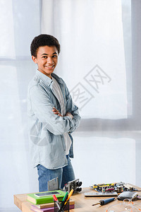 身着笑的非洲青少年站在家桌边手举横臂配有装备图片