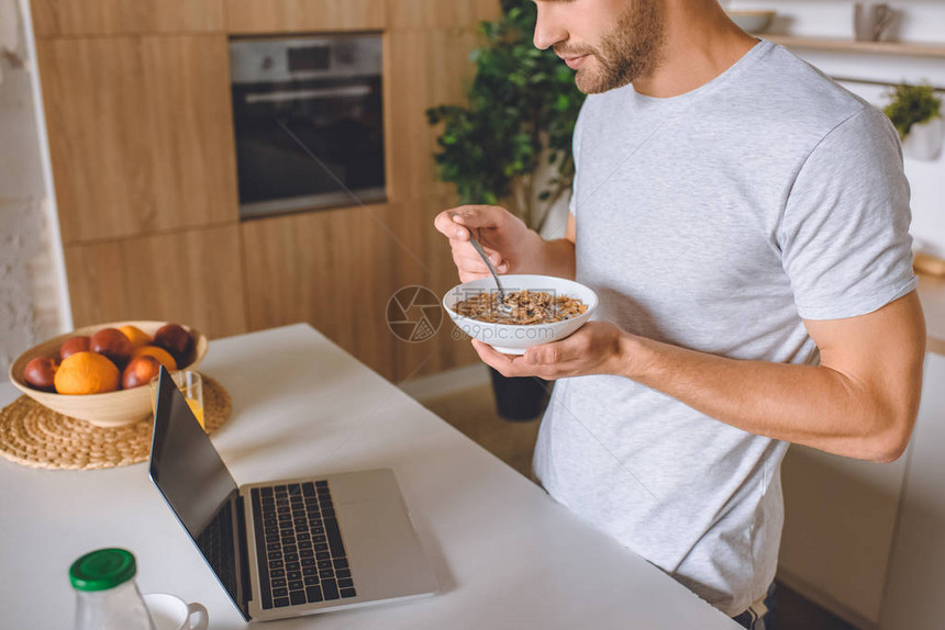 人类在早餐时用牛奶吃片子和看厨房笔记本电脑屏图片