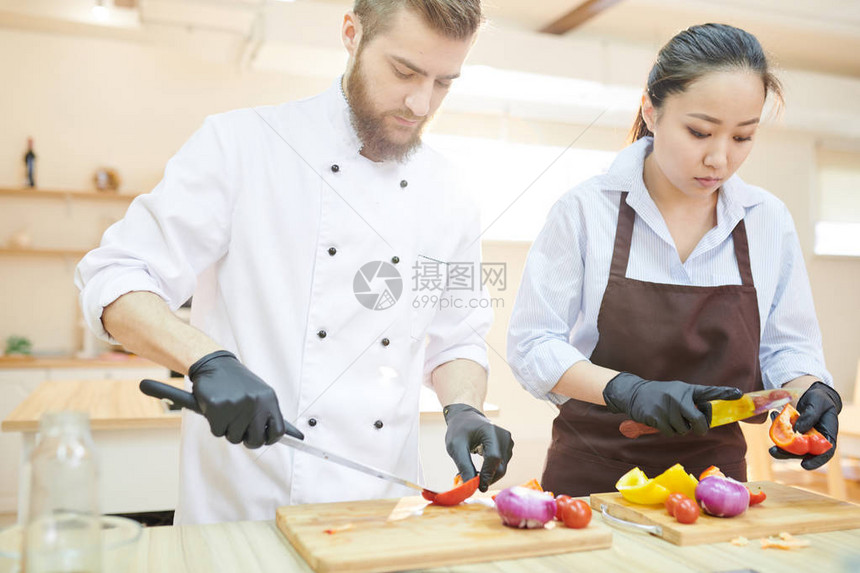 两位在餐厅厨房切菜的专业厨师站在木桌旁的腰部肖图片