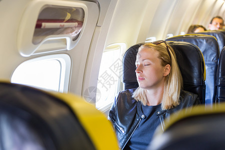 疲倦的金发美女随身带着飞机在窗边靠着后座睡觉脖子高清图片素材