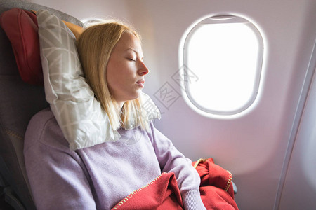 疲惫的金发休闲白种女人在长途跨大西洋航班上睡在座位上通过飞机疲劳的高清图片素材