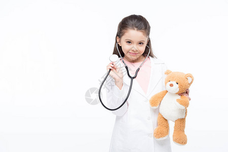 穿着医疗制服手持听诊器和泰迪熊的微笑小女孩图片