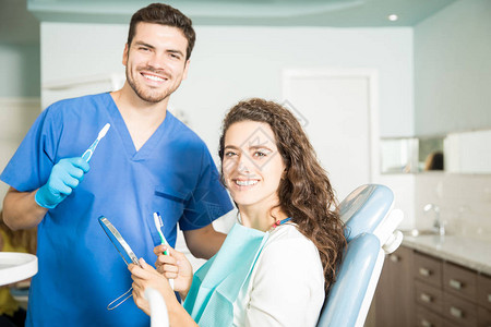 微笑的牙医和在诊所内持有牙刷和牙镜图片