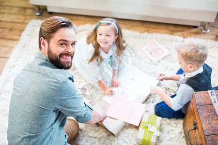 快乐的年轻父亲和两个孩子坐在地毯图片