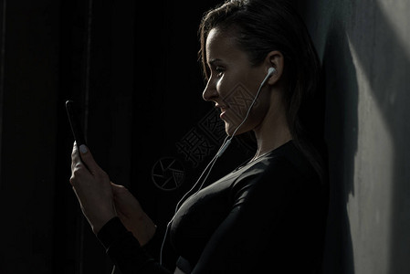 使用智能手机用耳听器微笑的年轻健身女背景图片