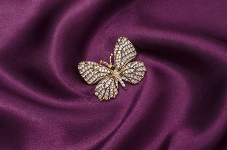 丝绸织物上镶有钻石的金蝴蝶胸针背景图片