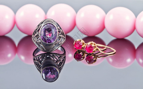 紫水晶银戒指和粉红色珠子背景上的红宝石金耳环图片