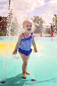 一个可爱快乐2岁的蹒跚学步的女孩在夏天的一天在外面玩水溅公园时弄图片