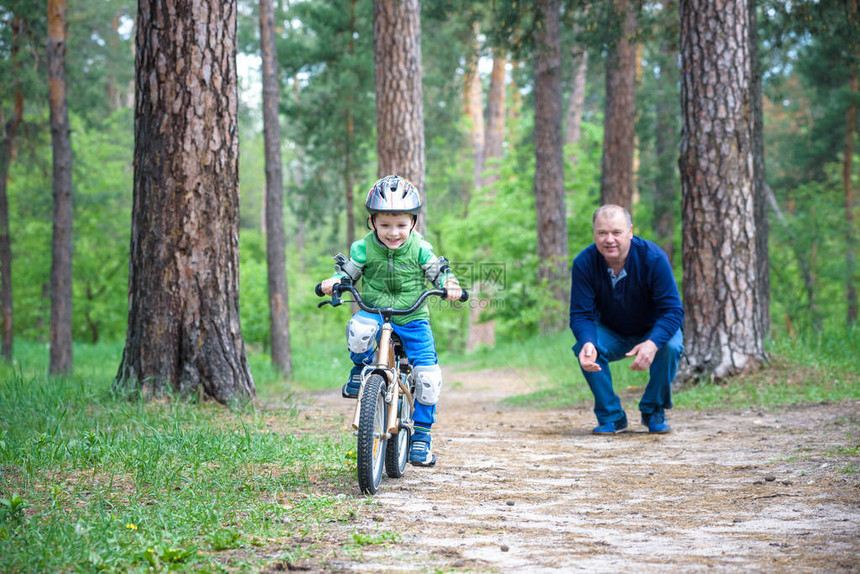 3岁的小男孩和他的父亲在秋天的森林里骑着自行车爸教儿子人对成功感到高兴带头盔的孩子安全运动休闲图片