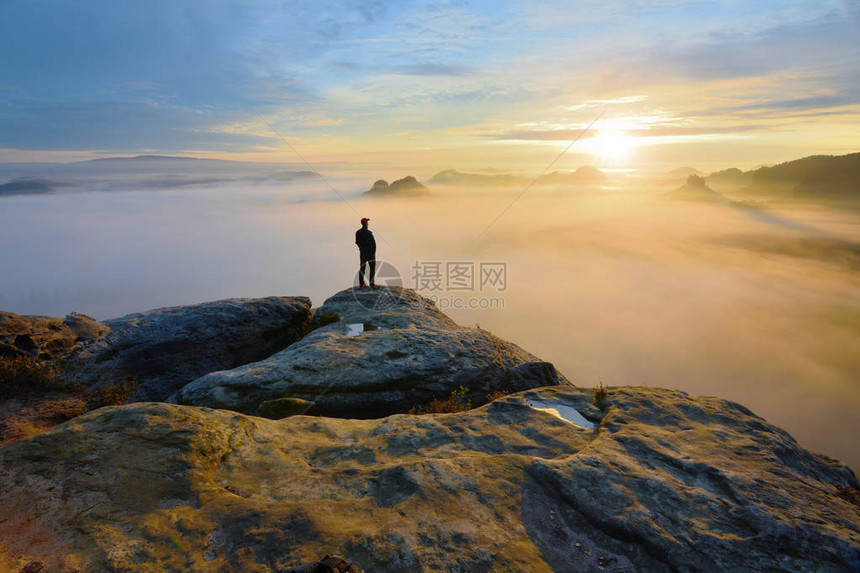 徒步旅行者在山谷上方的岩石尽头男人看着朦胧和秋天的早晨山谷到明亮的早晨游客正在寻找迷雾笼罩的山谷秋图片