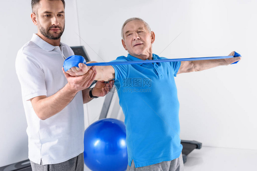 协助老年男子用橡胶带进行锻炼的康复治图片
