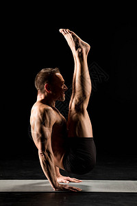 年轻的运动男子练习瑜伽在黑色隔离的瑜伽图片