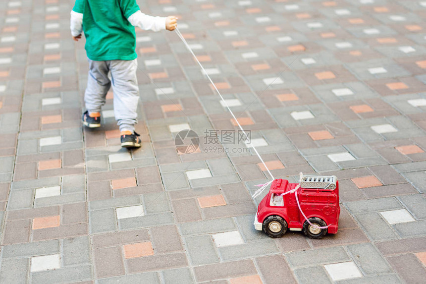 小孩在户外玩耍孩子拿着绳子带着红色消防车玩具卡车图片