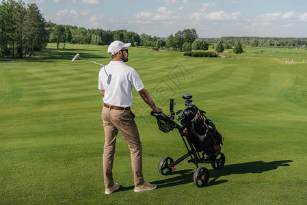 年轻高尔夫球手一边站在绿色球场上与袋和俱乐部站在一起图片