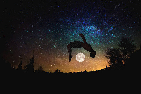 运动男子在夜晚星空和月亮背景时跳过圆图片