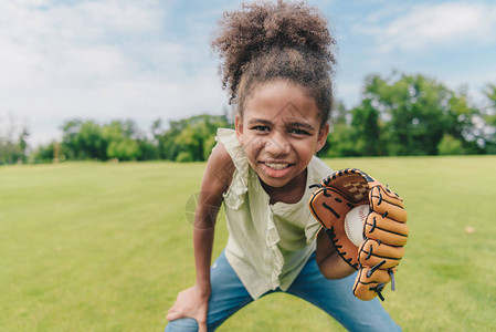 戴着棒球手套和在公园打棒球的非洲裔美国小女图片