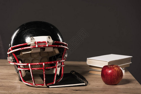 近视美国足球头盔教科书苹果和一堆灰色背景的书集Grey图片