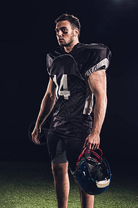 身穿黑色制服的美式足球运动员持有头盔仰图片