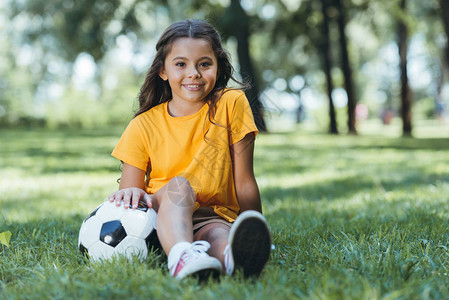 可爱的快乐的孩子坐在草地上足球图片