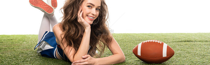 身着蓝色制服的微笑啦队长女孩躺在绿色球场上的橄榄球附近图片