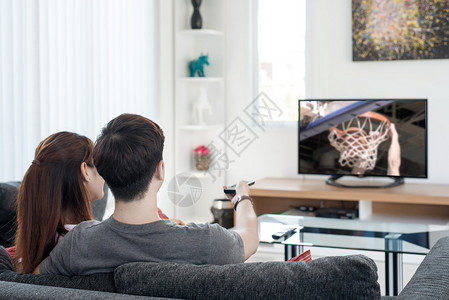 年轻亚裔夫妇在家看电视篮球比赛图片