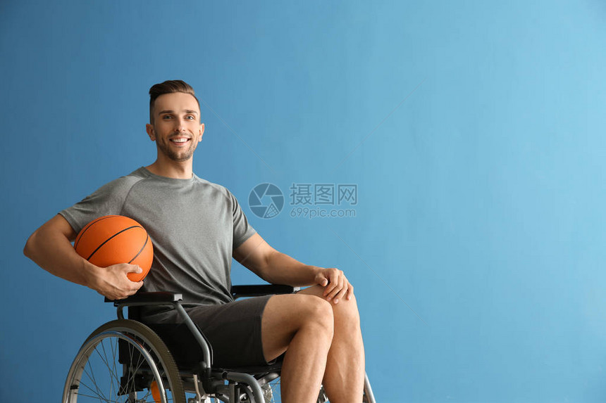 年轻篮球运动员在彩色背景下坐在轮椅上的青图片