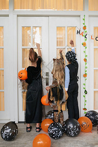 孩子们穿着漂亮的万圣节服装站在房子的门廊上敲门要背景图片