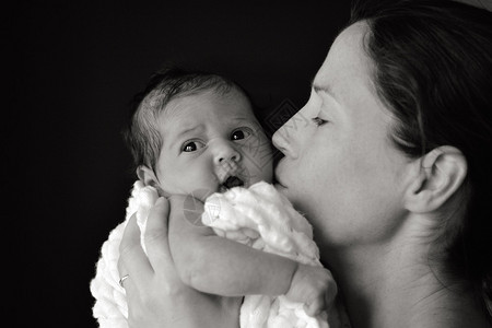 年轻母亲抱着并亲吻新生婴儿3周大图片