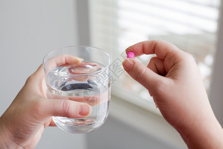 女人手拿着药丸和一杯水的形象图片