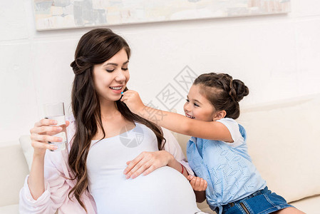 小女孩用一杯水喂给怀孕母亲吃药丸背景图片
