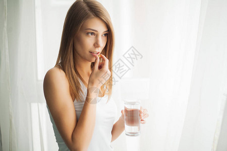 快乐的笑容积极的女人吃药丸和握着杯水在手背景图片