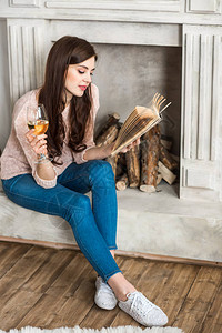 坐在壁炉附近阅读书和喝白酒的有吸引背景图片