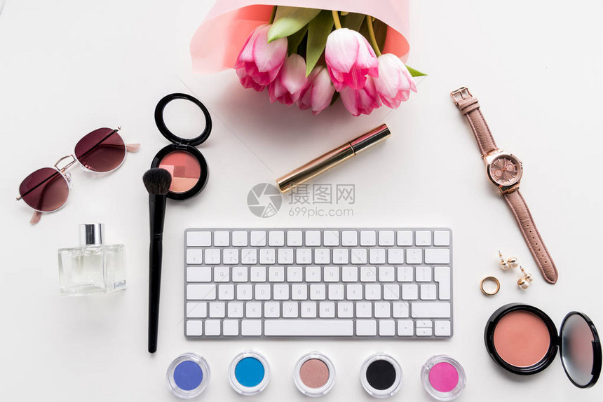 电脑键盘各种化妆品附件和花束上方的白色粉红图片