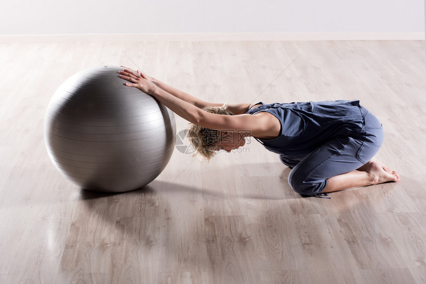 在硬木工作室地板上的银健身球顶上伸展的手臂伸展着肩膀的图片