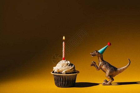 玩具恐龙在蛋糕旁边的派对帽在棕色背景图片