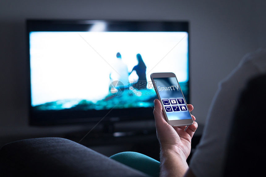 男人看电视和在手机上使用智能电视遥控器应用程序使用智能手机在菜单和用户界面中选择电影流切换频图片