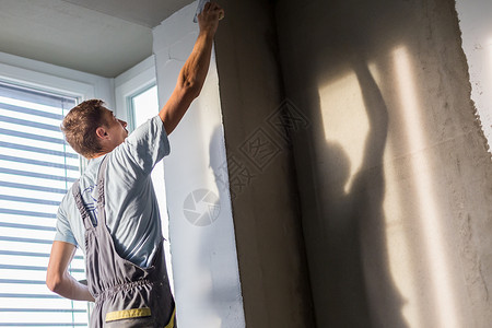 三十岁的体力工人在房子里用抹墙工具泥水匠用浮子和石膏翻新室内背景图片