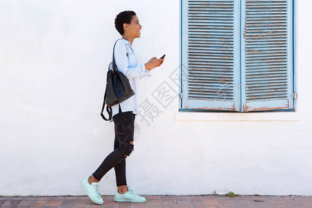 青年妇女用手机和手提袋行走的图片