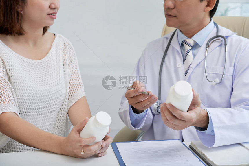 医生穿着白大褂坐在办公桌前给年轻病人开药图片