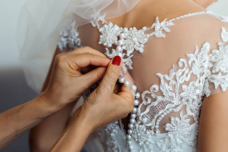 伴娘为婚礼准备新娘仪式前系好白色新娘礼服图片