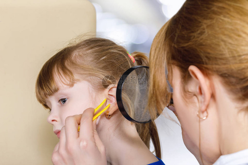 女儿科医生在用放大镜和tweezers检查一只耳朵时图片