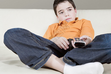 年轻男孩在家看电视坐在白皮沙发上时图片