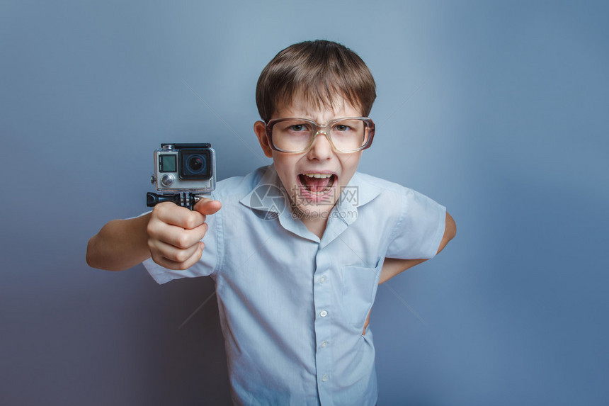 一个10年欧洲外貌的男孩戴眼镜拿着相机双手握着照相机在灰色图片
