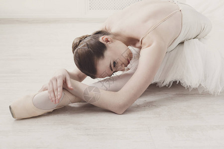 美丽优雅的年轻芭蕾舞女演员在白色木地板的足尖鞋使芭蕾腿伸展古典舞图片