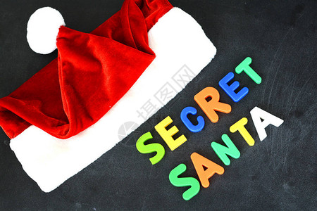 圣诞老人红色帽子附近的黑板上带有多彩磁字母的秘密背景图片