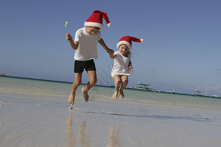 两个快乐的小孩戴着圣塔帽的孩子在自然热带背图片