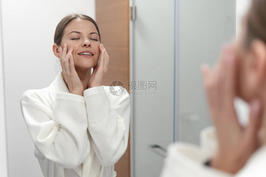 白浴袍中的年轻成人和美貌佳丽女子站在光亮的浴室里图片