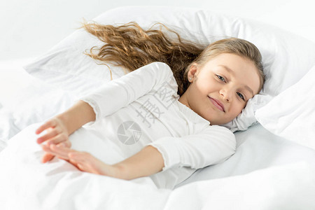 穿着白色睡衣的可爱小女孩在家中床上醒来图片